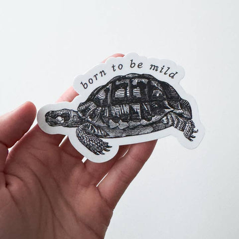 Hand holding a turtle-shaped sticker with 'born to be mild' text on a white background
