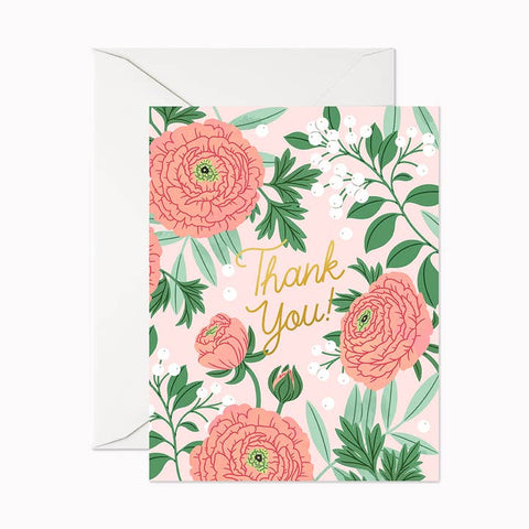 A floral thank you card with a white envelope behind it. The card has a light pink background decorated with coral-pink flowers, green leaves, and gold cursive text reading 'Thank You'.