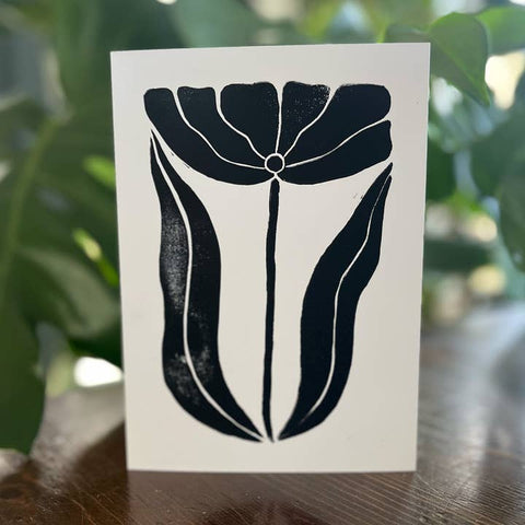 Card with black floral design on a white background, placed outdoors.