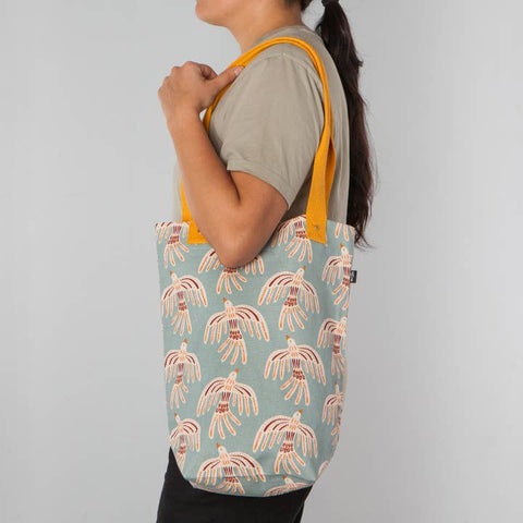 Person holding a tote bag with a pattern of birds on a light blue background