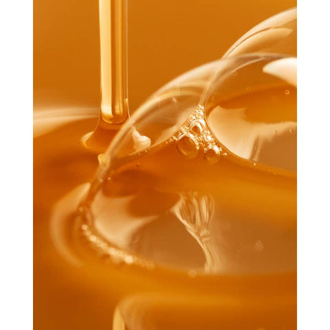 Close-up of a dropper with liquid being dispensed into a clear container on an orange background
