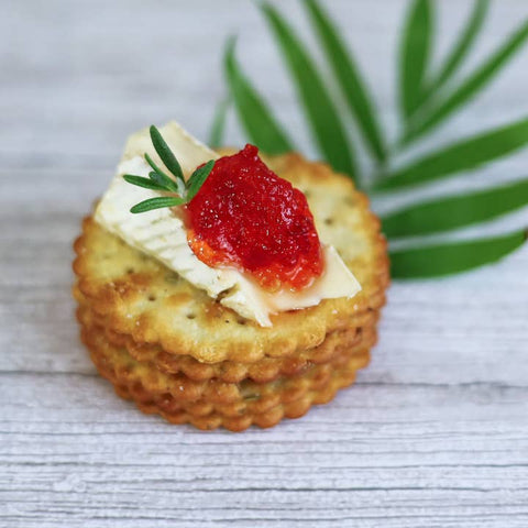 Cracker topped with cream cheese, red sauce, and a sprig of rosemary on a wooden surface.