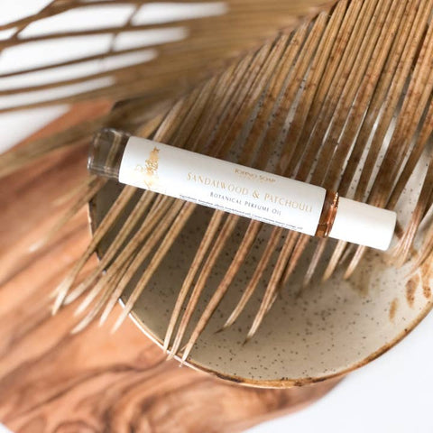 Roll-on bottle of Sandalwood & Patchouli essential oil on a textured ceramic plate with dried palm leaves.