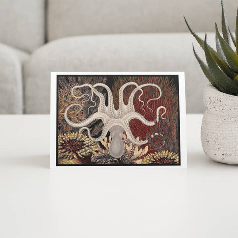 Decorative card with an octopus design on a table with a plant in the background