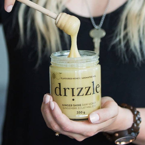 Person holding a jar of Drizzle honey with a wooden dipper.