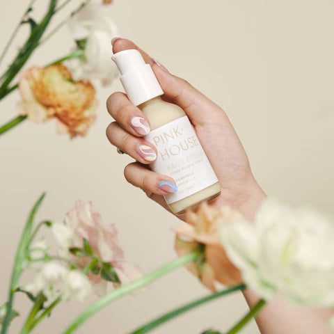 Hand holding a bottle labeled 'Pink House' with flowers in the background