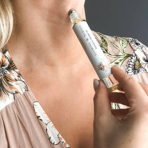 Person applying a perfume spray to their neck with a floral-patterned dress.