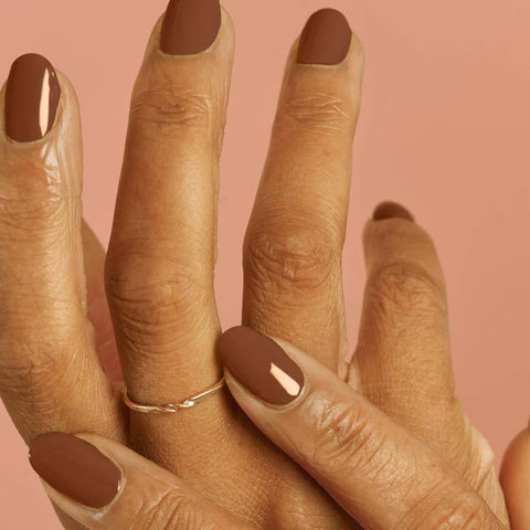 Close-up of a hand with brown nail polish on a pink background