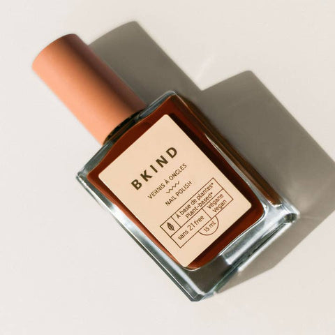 Nail polish bottle with 'BKIND' label on a neutral background