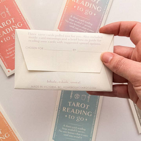 Hand holding a tarot card envelope with tarot cards in the background