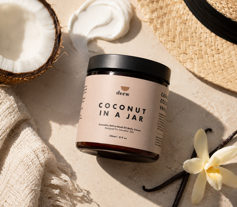 Jar of coconut body cream with a vanilla flower and coconut on a beige background