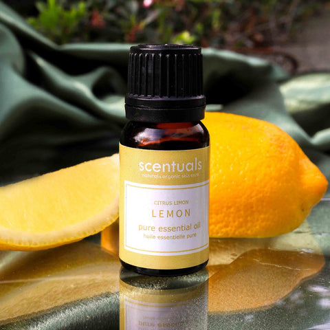 Scentuals lemon essential oil bottle with lemons on a reflective surface