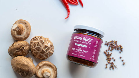 Shiitake mushrooms and a jar of Umami Bomb Shiitake Chilli Oil on a white background