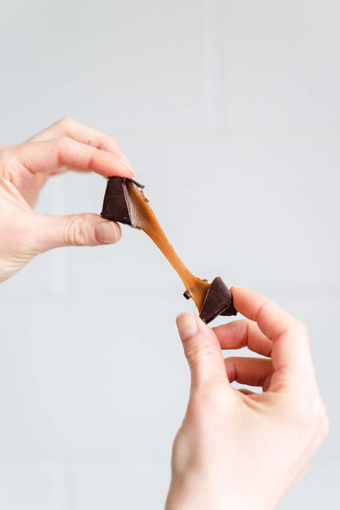 Hands holding a chocolate-dipped caramel against a light gray background