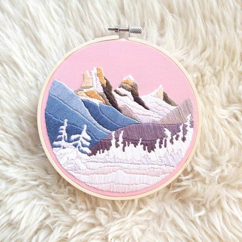 Embroidery hoop with a mountain landscape design on a fluffy white surface
