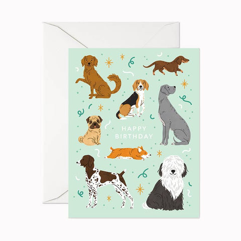 A birthday greeting card featuring illustrated dogs on a pale mint background with the words 'HAPPY BIRTHDAY' in the center, shown with a white envelope behind it.