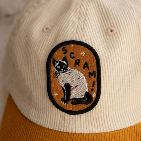 Cap with a cat patch and 'SCRAM!' text on a beige and orange background