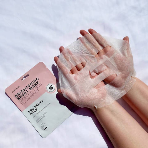 Person applying a brightening sheet mask to their hands with the packaging visible.