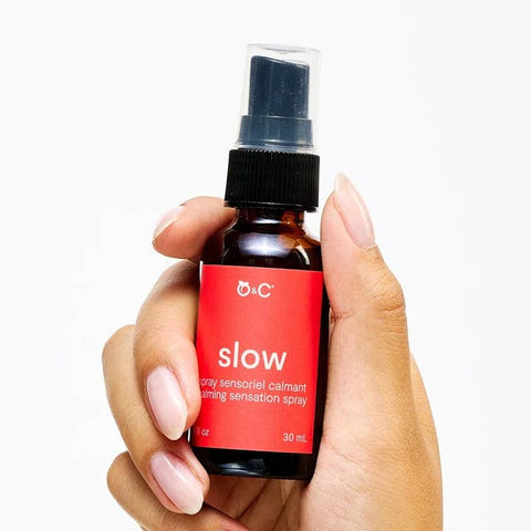 Hand holding a bottle of 'slow' spray with a red label on a white background