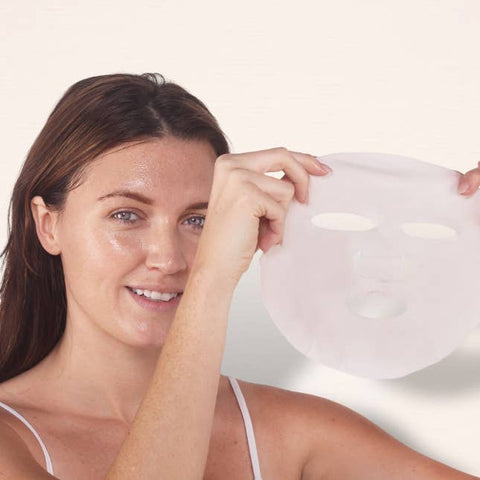 Woman holding a white face mask against a plain background