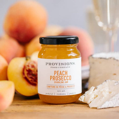 Jar of Provisions Food Company Peach Prosecco Sparkling Jam with peaches in the background