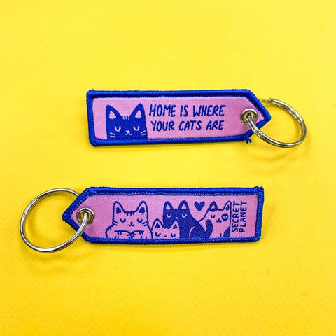 Two keychains with cat illustrations and text on a yellow background