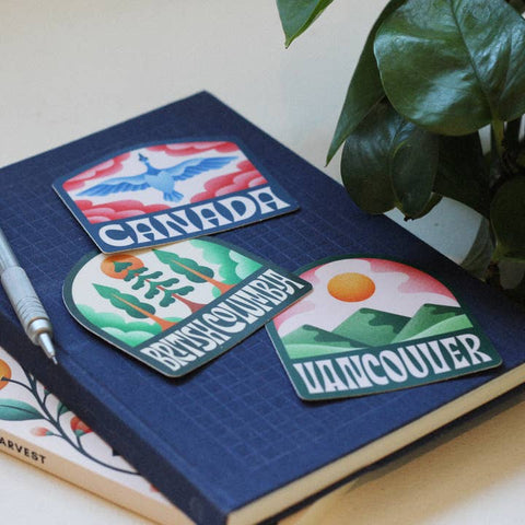 Three decorative stickers on a notebook with a plant in the background