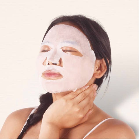 Woman applying a white facial mask on a plain background