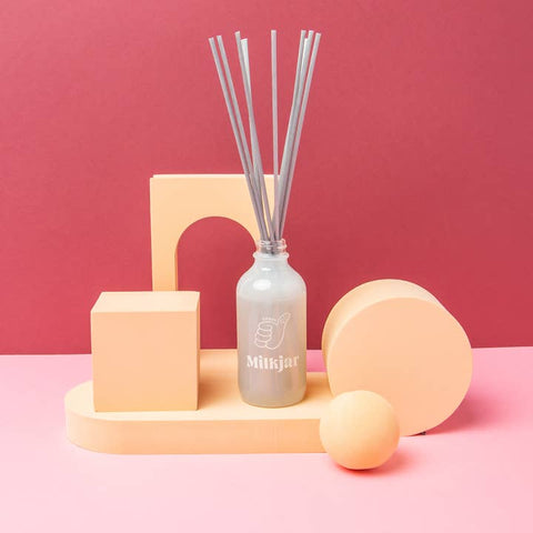 Diffuser with reeds on a pink platform against a pink background, featuring the brand 'Milkjar'.