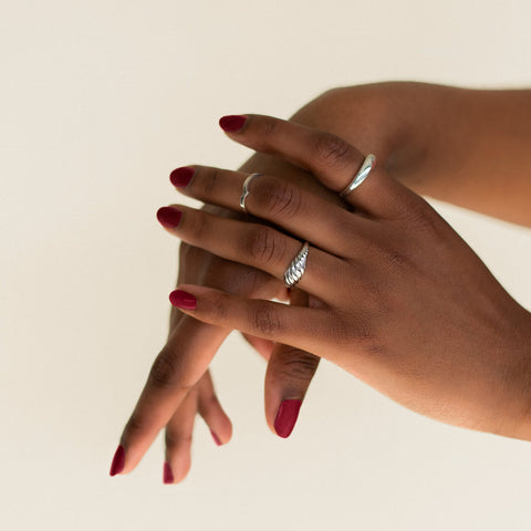 Close-up of two hands with red nail polish wearing silver rings on a beige background