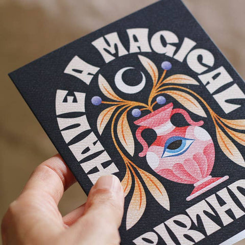 Hand holding a card with a magical birthday design featuring a heart and text.