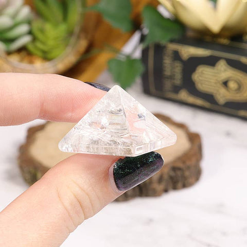 Person holding a clear crystal pyramid with plants and a book in the background