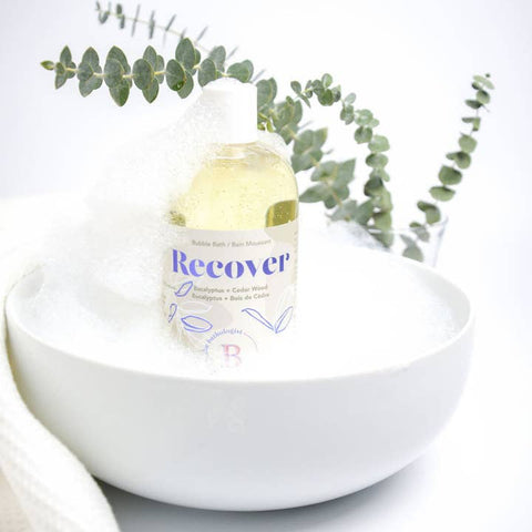Bottle labeled 'Recover' in a white bowl with eucalyptus leaves on a light background