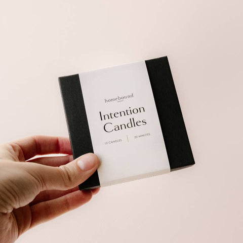 Hand holding a box of 'Intention Candles' by homebound on a light background