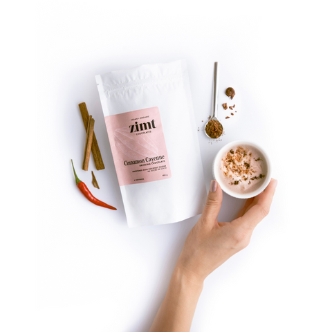Hand holding a small bowl of cinnamon spice mix with a package labeled 'zimt' on a white background.