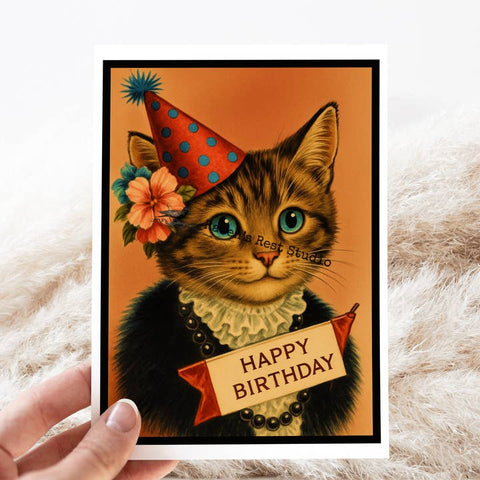 Birthday card with a cat wearing a party hat and holding a 'Happy Birthday' sign, held by a hand on a textured surface.