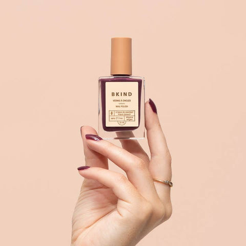 Hand holding a bottle of BKIND nail polish against a beige background