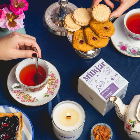 Tea time setting with cookies, tea cup, and 'Milkjar' products on a table.