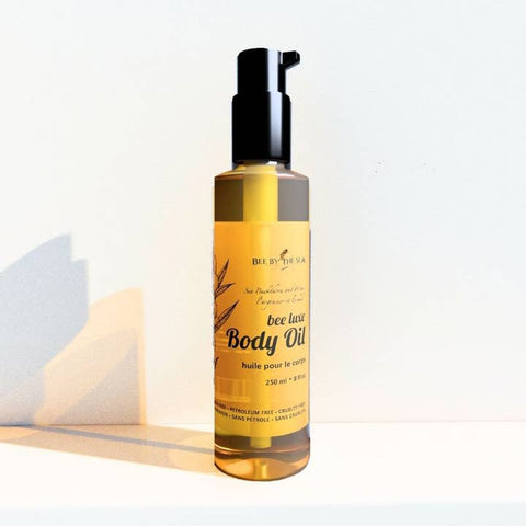 A bottle of bee lust Body Oil by Bee by the Sea, featuring a black pump dispenser and a yellow label, set against a plain white background with a soft shadow.
