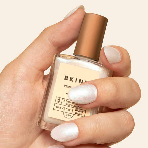Hand holding a bottle of BKIND nail polish with a neutral background