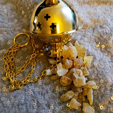 Gold incense burner with chain and copal resin on a textured surface