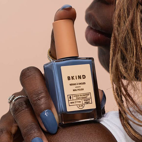 Person holding a bottle of BKIND nail polish with visible brand name.