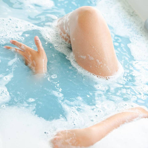 Person's legs and feet in a bubble bath with blue water