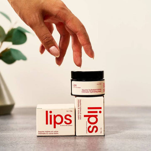 Hand reaching for a container labeled 'lips' on a neutral background