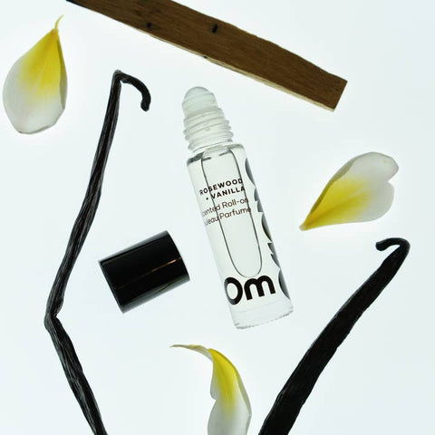 Roll-on perfume bottle with vanilla bean and flower petals on a white background