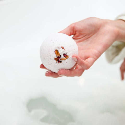Hand holding a white bath bomb with dried herbs against a light background
