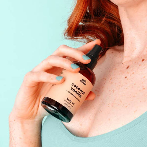 Person holding a bottle of coconut vanilla body oil against a light blue background