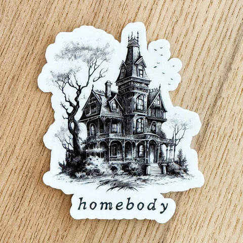 Sticker of a black and white Victorian house with 'homebody' text on a wooden surface