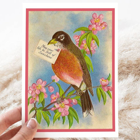 Vintage-style greeting card with a bird and cherry blossoms, held by a hand.