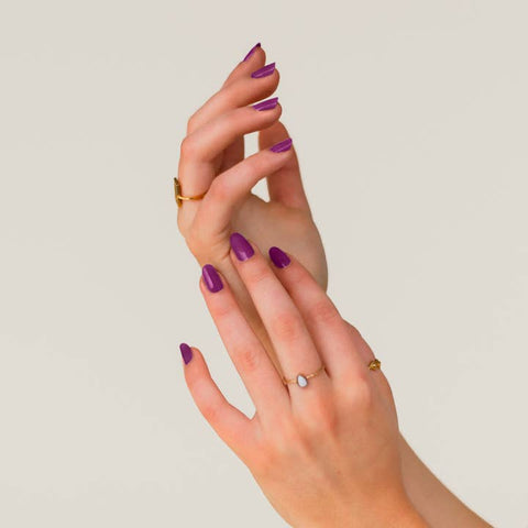 Close-up of a hand with purple nail polish and gold rings on a plain background